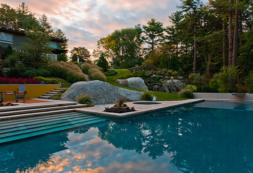 Deep blue pool reflects the sunset and is surrounded by a custom stamped concrete pool deck and huge boulders constructed from concrete.