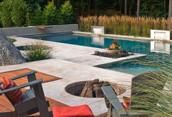 Modern clean pool deck surrounds a glistening swimming pool and deep fire pit.