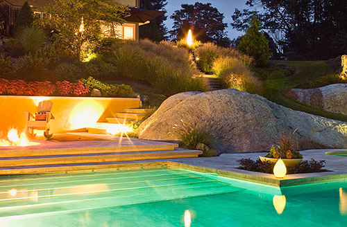 Large boulders created from concrete surround a large swimming pool accented by stamped concrete pool deck.