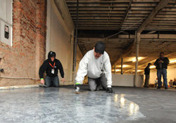 Two men trowel the metallic epoxy on the floor of the abandoned building.
