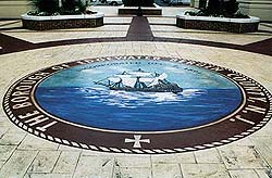 Concrete overlay circle logo of a ship on the blue ocean states "the borough of Edgewater Hergen County NJ" has a stamped patterned concrete around the smooth logo area.