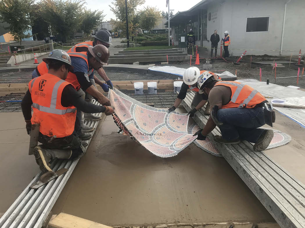 Contractors placing the lithomosaic salmon on the concrete.