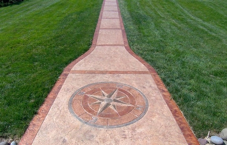 A long concrete pathway with a stained compass rose making its way through green grass.