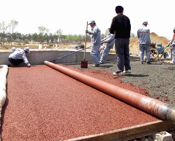 In China, workers install an integrally colored pervious wear course. They are laying the pervious concrete over a structural course that was placed just 20 minutes earlier.