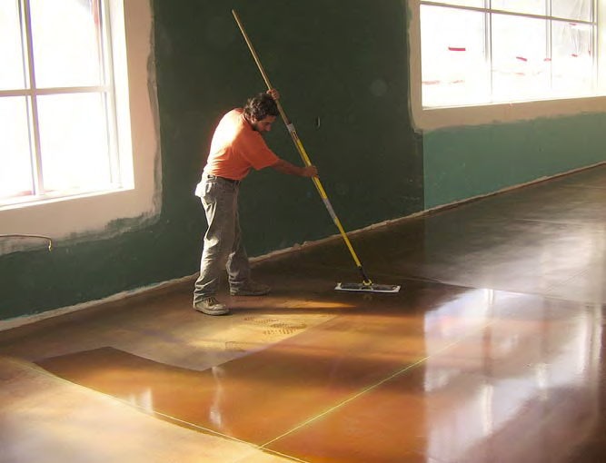 Contractor applies floor coating with a large broom.