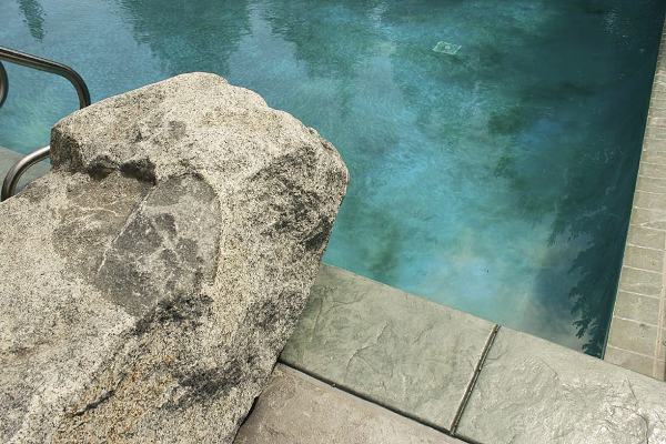 A faux rock up against the edge of the pool water acts as a diving board from the pool deck.