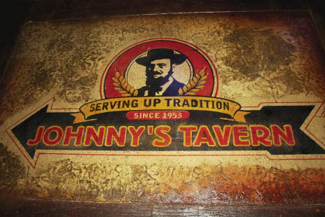 A Johnny's Tavern logo stenciled and colored on brown stained concrete.