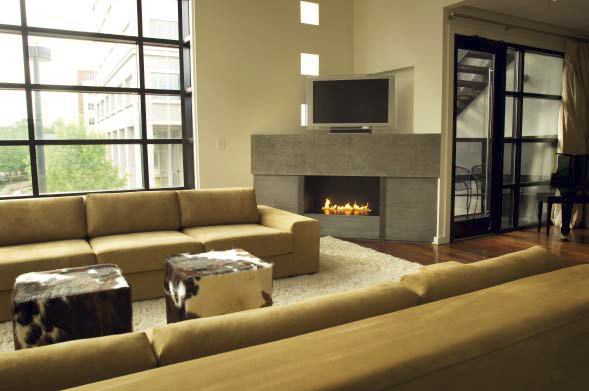 A concrete fireplace with a flat screen television on top of it in a room with two couches and cow skin covered ottomans. 