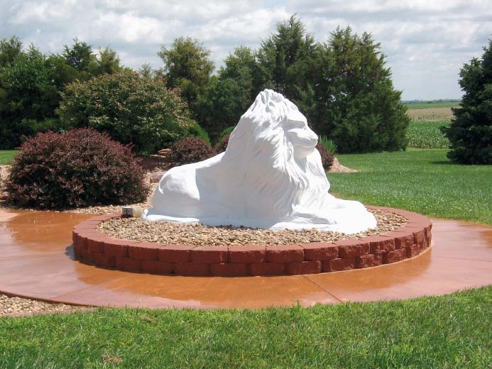 White concrete lion sits upon a decorative concrete colored concrete circular pad.