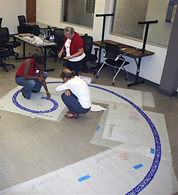 Milena Sellers-Phillips (left) and Maria Keever (rear) add personal touches to the mosaic Fibonacci spiral as Amanda Klemaske Conahan looks on. In the LithoMosaic system, the mosaic is created off-site on mesh, then embedded in the concrete. The mothers placed the mementos on the mesh right side up, and Conahan turned them upside down before gluing.