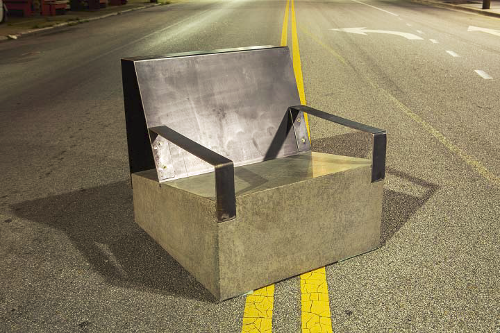 A concrete chair with metal arm rests sitting in the middle of the highway.