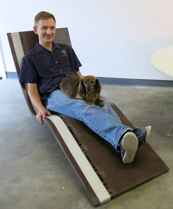 Jeff Girard sits on his thin cast concrete lounge chair with his dog.