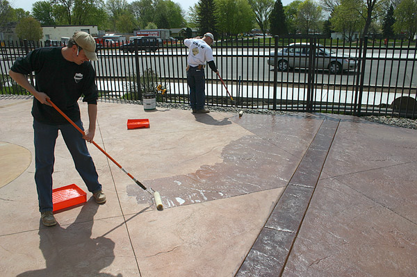 Two crew members are applying to sealer on concrete - drying sealers vs curing sealers