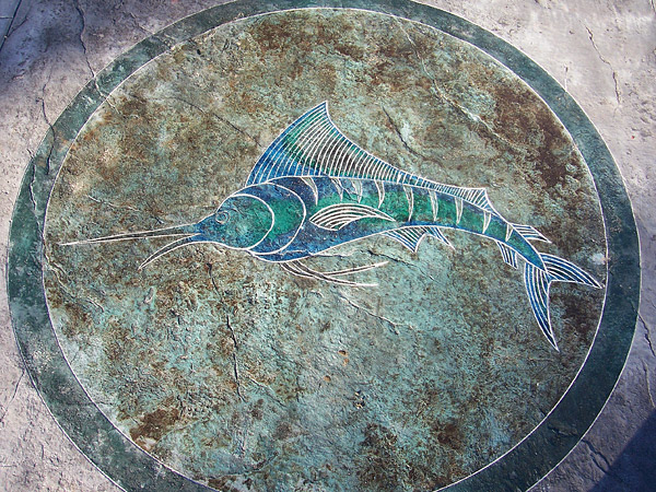concrete artists use color wheel to create blue green marlin swordfish within circle on brown textured concrete floor.