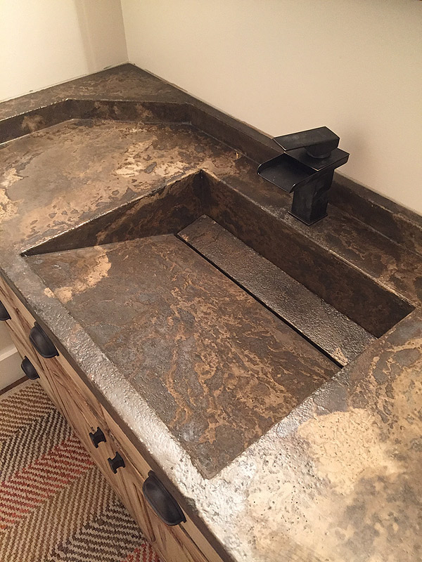sloped integral concrete sink in dark brown and tan colors and a rubbed bronze faucet.