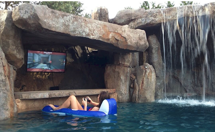 Playing video games while floating in a pool that is surround by vertically carved concrete and a waterfall.