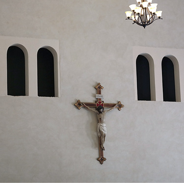 Crucifix hangs on a seminary wall below six arched openings coated with a polymer modified concrete coating made by Pure Texture. 
