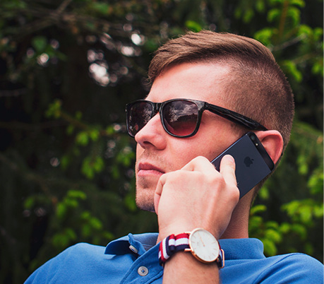 Manscaped man with stylish sunglasses using a cell phone outdoors near a tree.