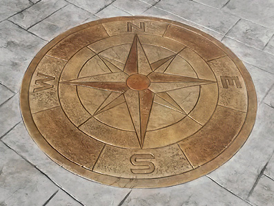 Stamped concrete compass pattern stained a darker color than the stamped concrete surround.