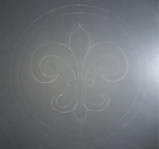 A finished chalk drawing of a fleur-de-lis on a concrete floor ready to be stained with water-based concrete stain.