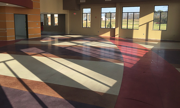 A large room with lots of windows showing off multiple colors in concrete on the floor.