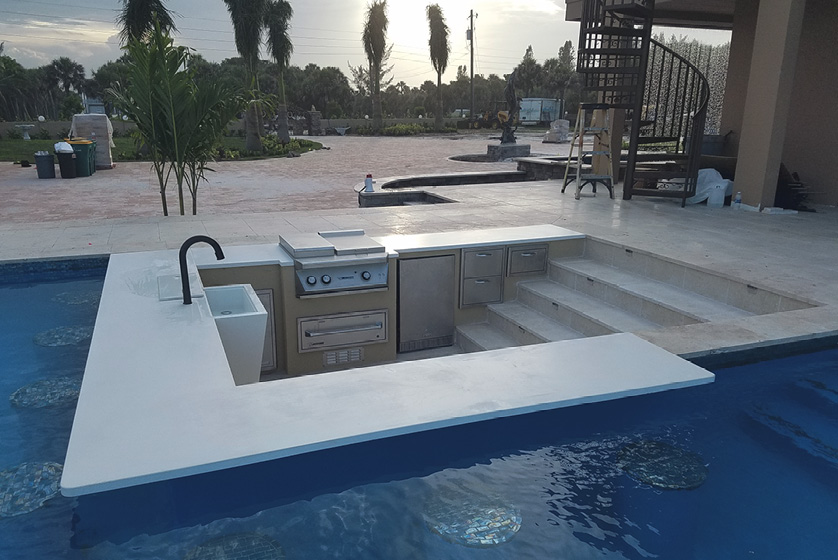 Cool sunk-in kitchen attached to a swimming pool where the concrete bar top hangs over the pool.