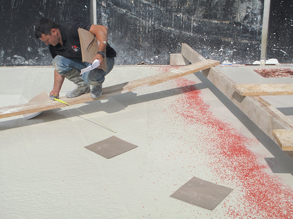 Concrete contractor placing stencil in pure white cement overlay spiked with red glass aggregate.