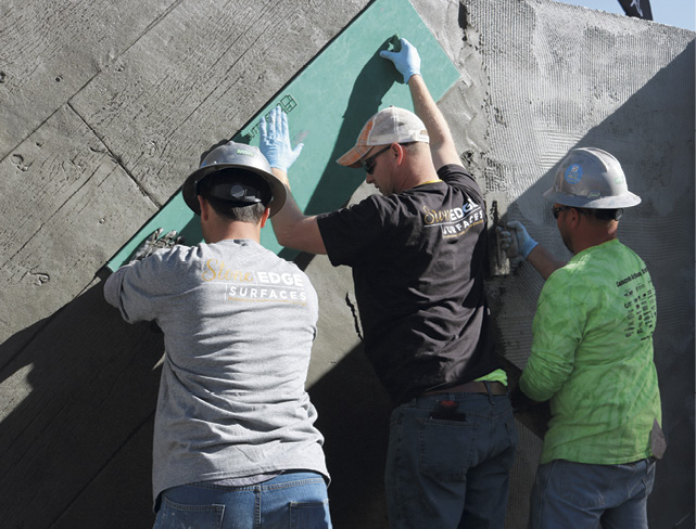 Three gentleman holding up a stamp to create would looking vertical concrete wall at Concrete Decor's Decorative Concrete Live at World of Concrete 2018.