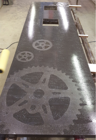 Deep gray integrally colored concrete countertop with embedded metal gears.