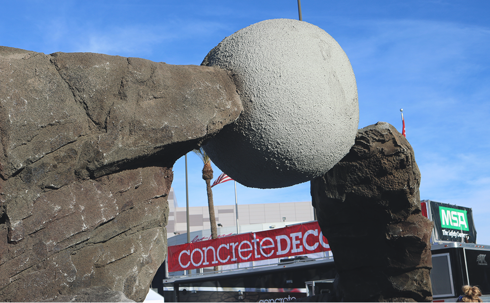 A sphere suspended between two rock features covered in concrete ready to be carved.