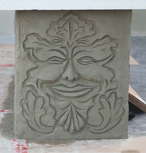 An artistic and whimsical face carved into the end of a concrete countertop.