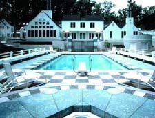 Black and white checkerboard concrete pool deck with diving board and large white house.