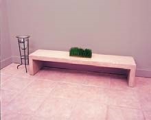 Precast tan concrete bench sits in a hallway with tile floor.