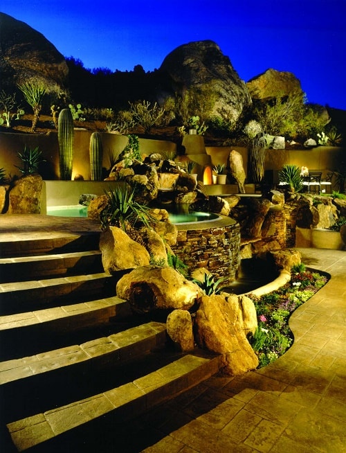 Boulders line a stamped concrete patio and stamped concrete stair treds near a misty spa on an Arizona hillside.