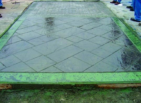 Dark green and light green stamped concrete slab with a green splotchy border showing pigmented color release after stamping a concrete slab.