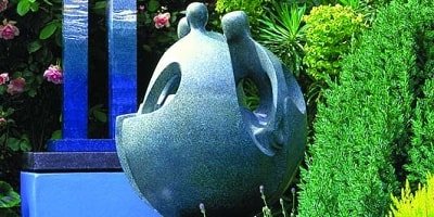 A concrete sculpture in a garden of what looks like people morphing into a sphere with heads facing each other.