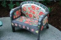A concrete chair outdoors that has been colored and decorated with a floral design.