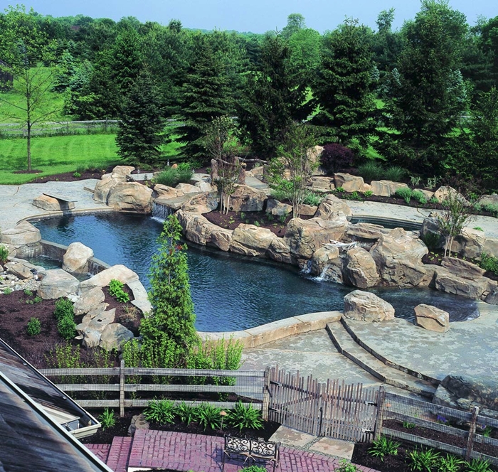 A large scale pond area that is flanked with faux rocks and rustic fences.
