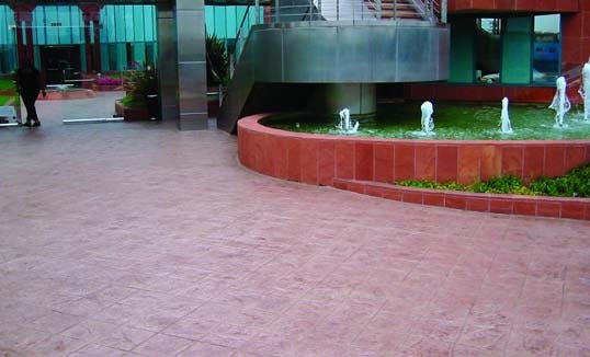 Brick red concrete overlay near a fountain with a red retaining wall.