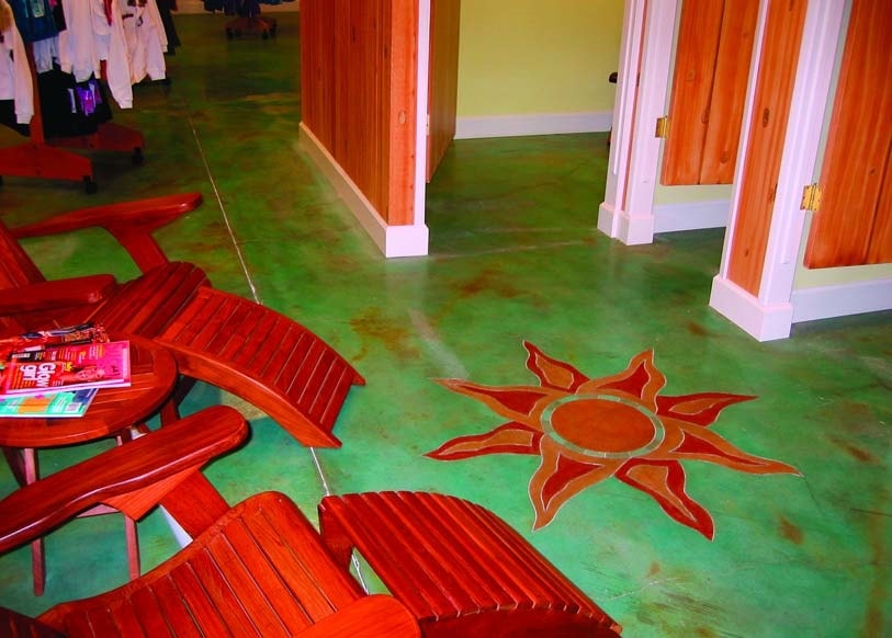 Redwood lounge chairs beside a busy clothing store dressing room where the floor is a blue green colored concrete overlay with a detailed sun that has been coating in a contrasting orange tan and red acrylic concrete stain.