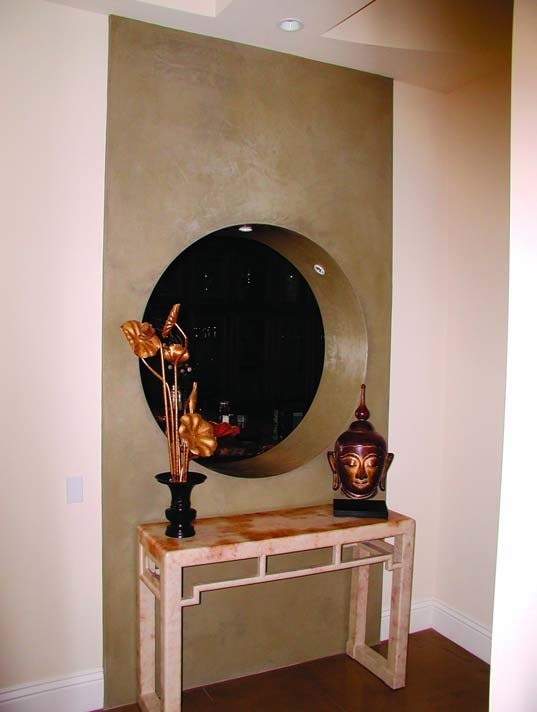 Entry to a high end home with a concrete vertical overlay featuring a circle cutout in the wall and recessed lighting to project mystery.
