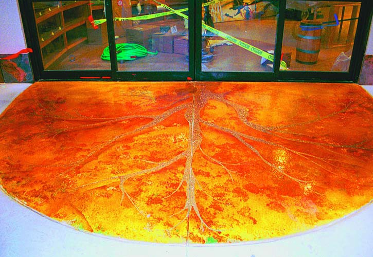 The entrance of a building is met with concrete imprinted and stained with the veins of a tree.