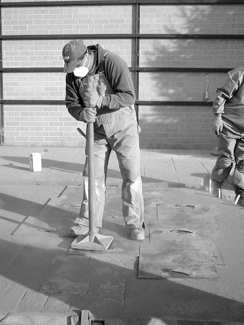 Concrete Stamping in cold weather tamping a stamp down with a long handled tamper while wearing appropriate safety gear.