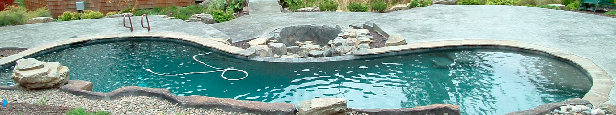 long pool surrounded by concrete rocks and a concrete deck that is stamped and textured.