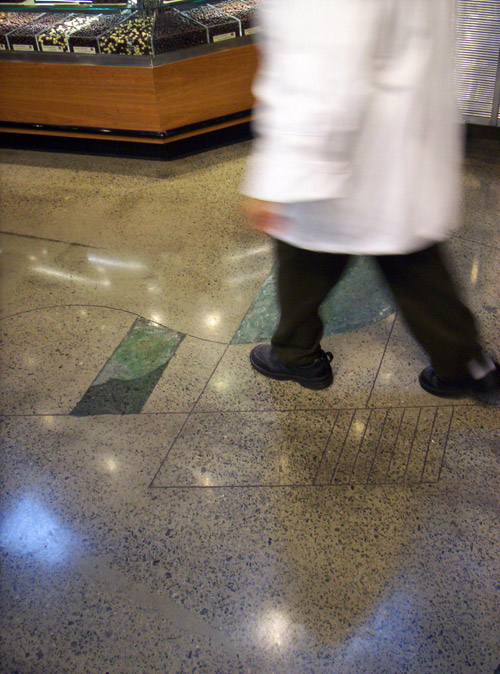 Butcher in a white coat walking across a polished and dyed concrete floor.