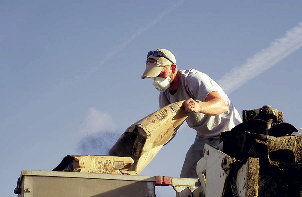 Particulate matter can be extremely harmful when inhaled. This picture shows a man dumping concrete mix into a hopper while wearing a dust mask.