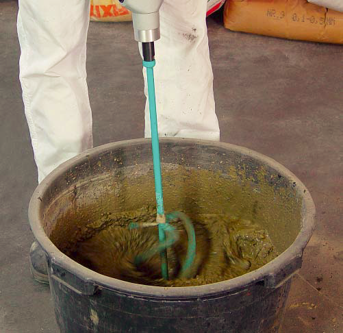 Using a hand mixer to mix concrete in a black bucket.