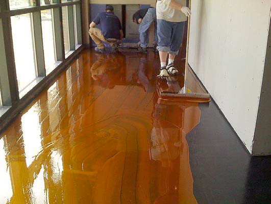 Pushing the stain along the concrete floor with a broom is an easy way to apply the concrete stain.