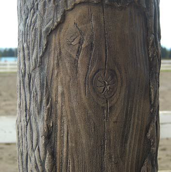 Verticaly carved concrete shaped into a log with missing bark pieces.