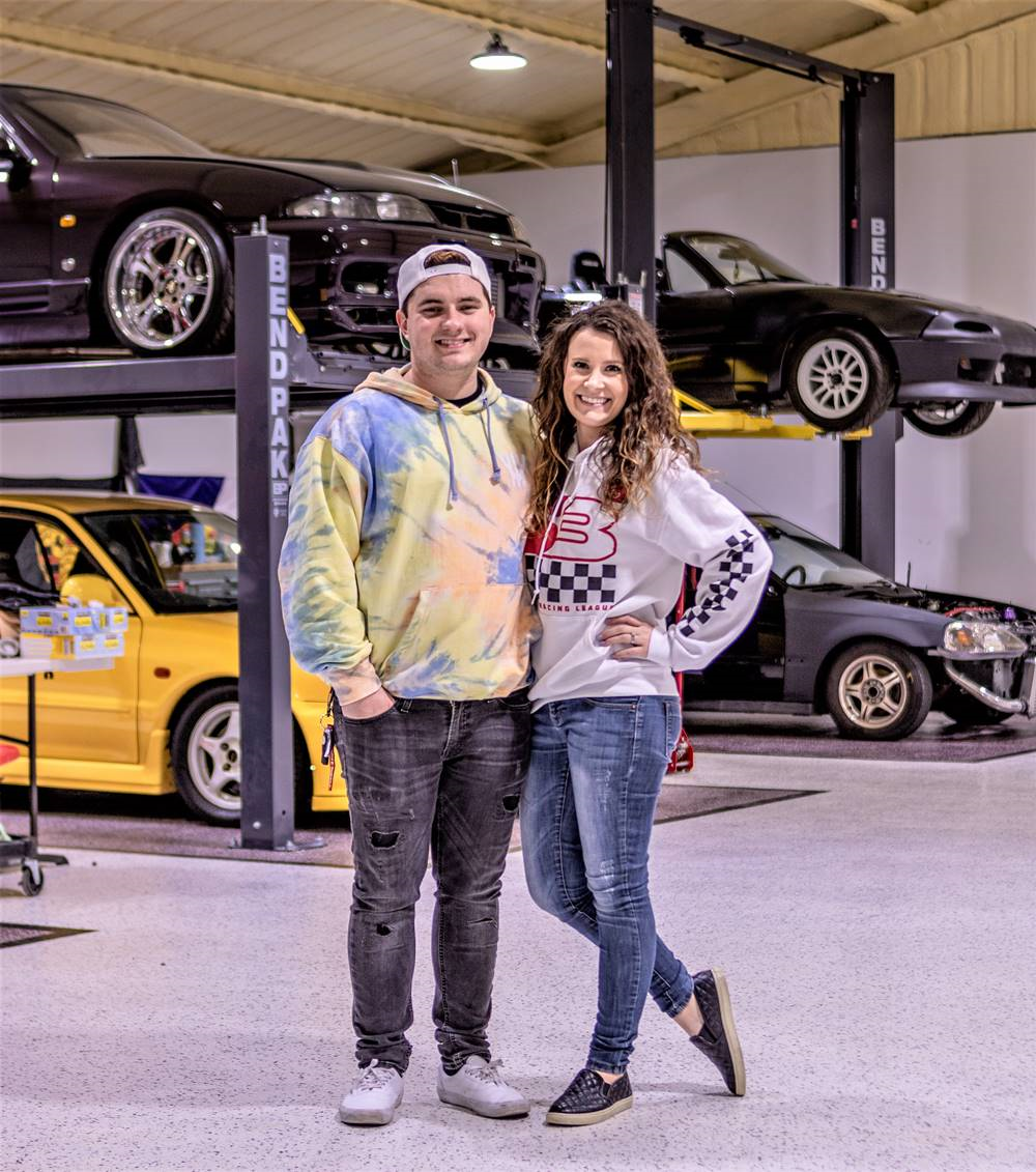 Evan and Victoria Shank in their garage in front of some custom cars